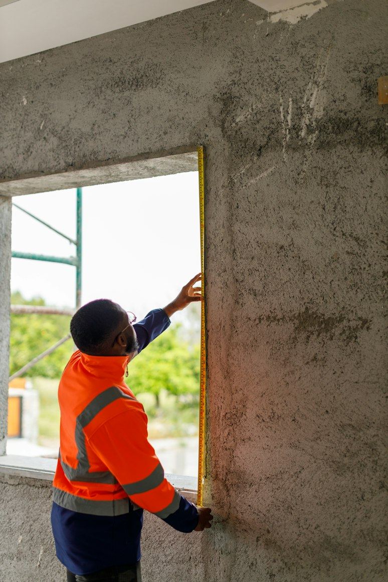 Builder in hi-vis measuring a window opening (illustrative)